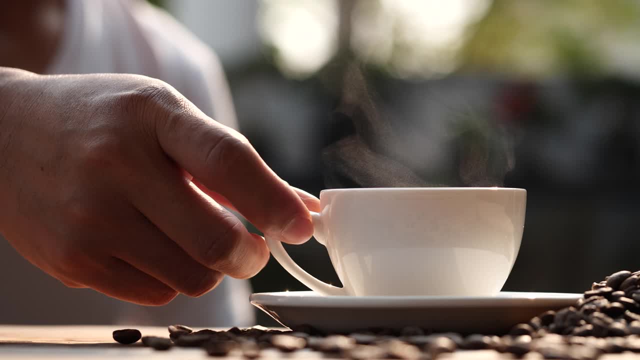 男人的手拿着热咖啡杯和咖啡的自然蒸汽烟放在木桌上，慢动作。热咖啡饮品概念。视频素材