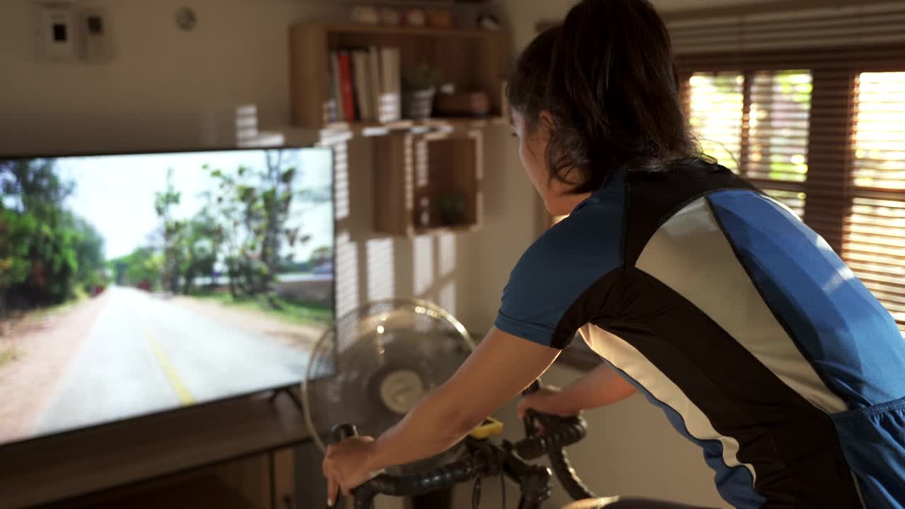 亚洲女人骑自行车。她在家锻炼。她在虚拟世界里玩游戏。视频下载