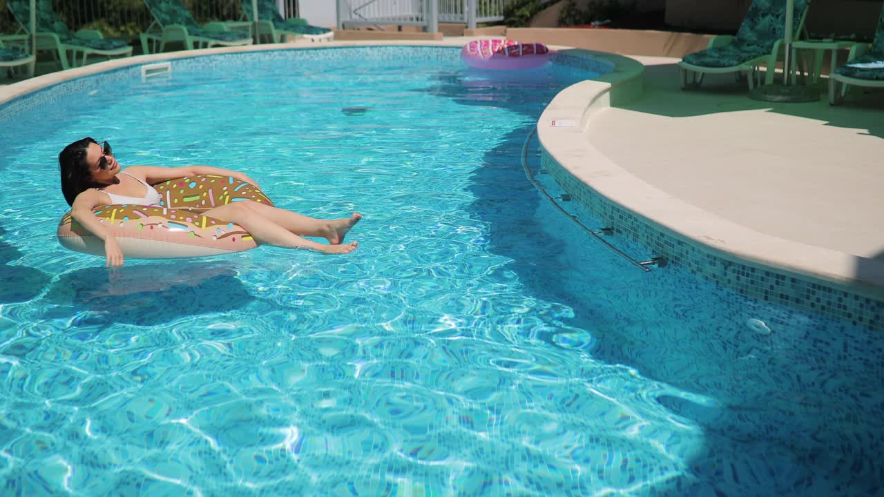 年轻女子在泳池边的充气甜甜圈上休息视频下载