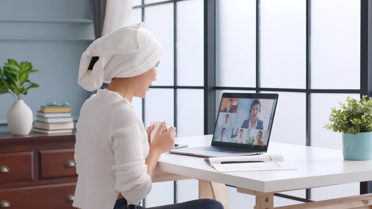年轻的亚洲湿发缠着头巾的女商人在家工作，与同事进行虚拟视频会议，在线工作，在家里进行视频通话视频素材