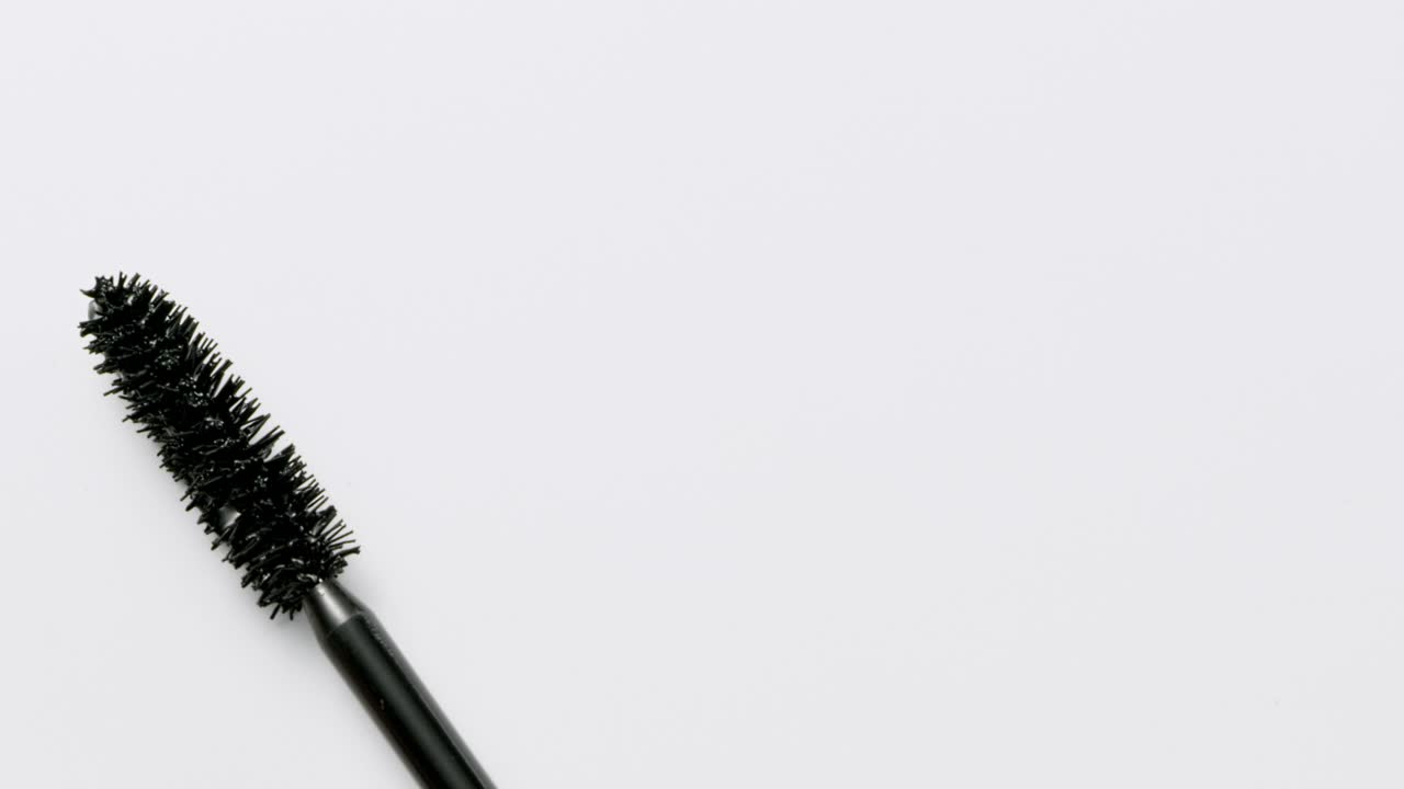 近距离和慢动作的黑色睫毛膏创造了一个睫毛膏棒在白色的背景视频素材