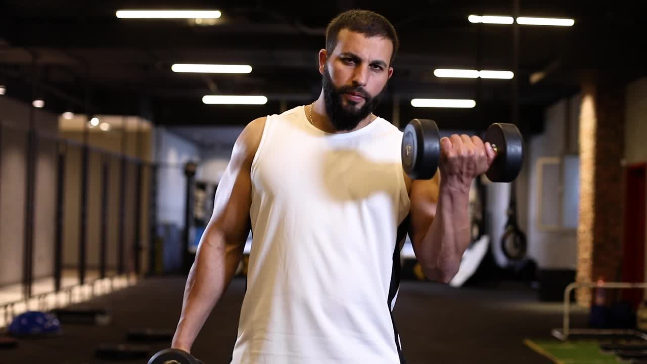 一个男人在健身房里用哑铃做二头肌屈身运动。视频下载