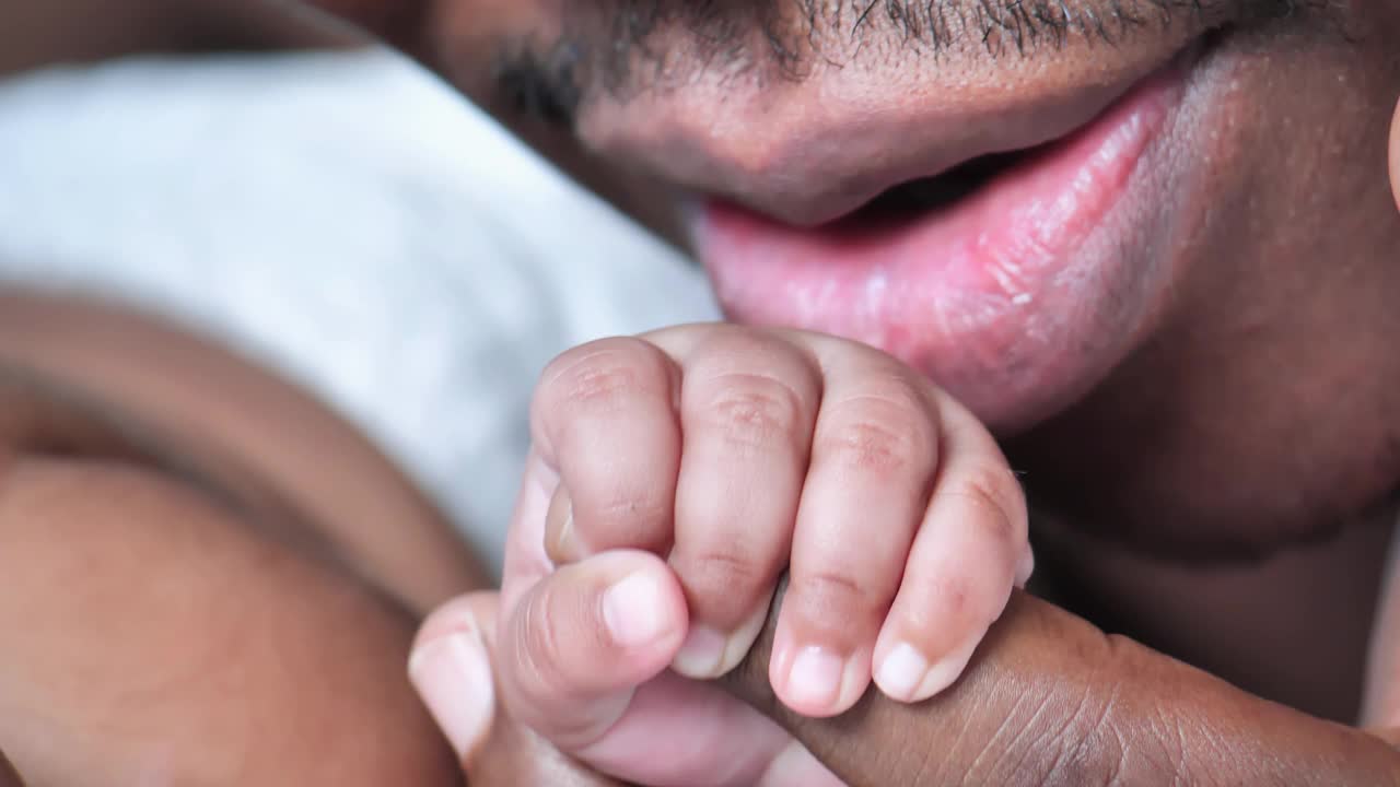 特写，快乐的非洲父亲种族，新生儿3个月时，她正在睡觉，亲吻她的手，手拉着手。家人时刻的概念。视频下载