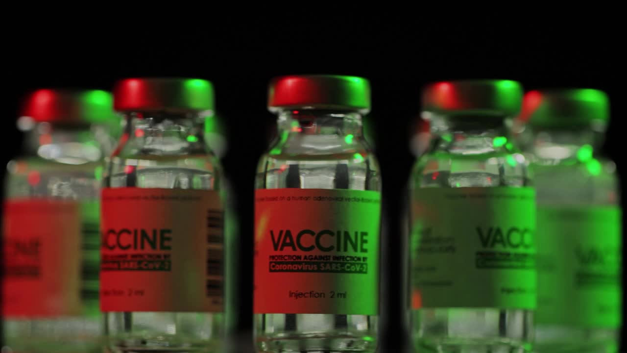 在红光和绿光下缓慢旋转用于治疗COVID-19冠状病毒的疫苗瓶。疫苗接种、注射、大流行期间的临床试验。瓶子，瓶子在黑暗中顺时针旋转视频素材