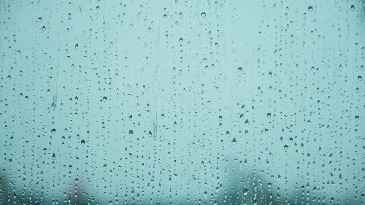 近距离观看雨滴滴在玻璃表面与蓝色背景。大雨时流下的水滴。视频素材