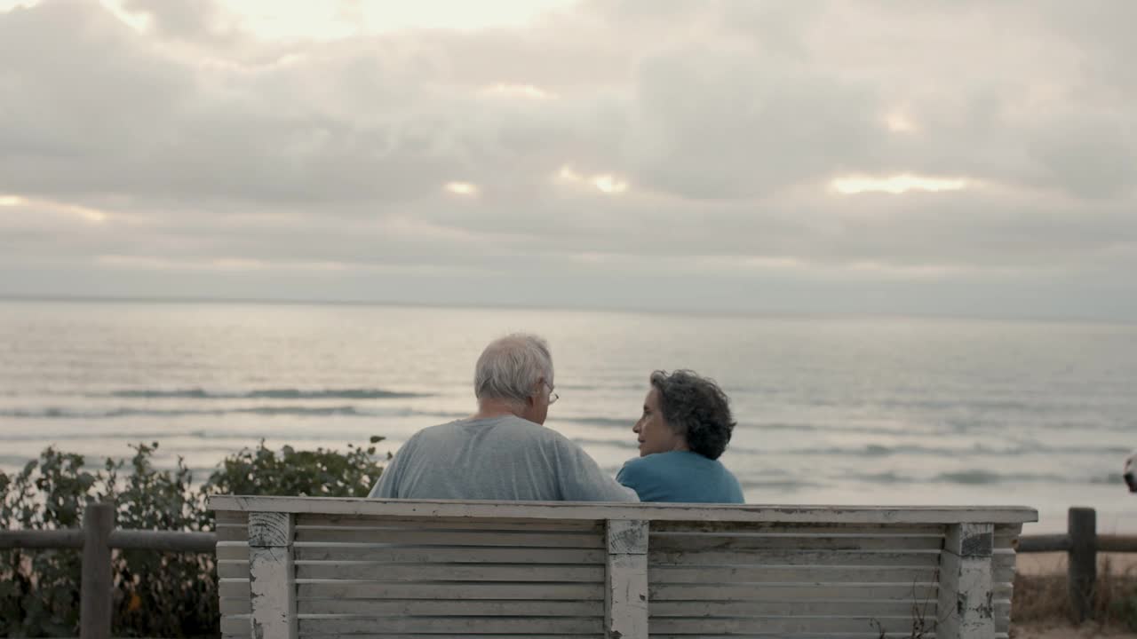 一对老年夫妇在海滩的长椅上看日落视频下载