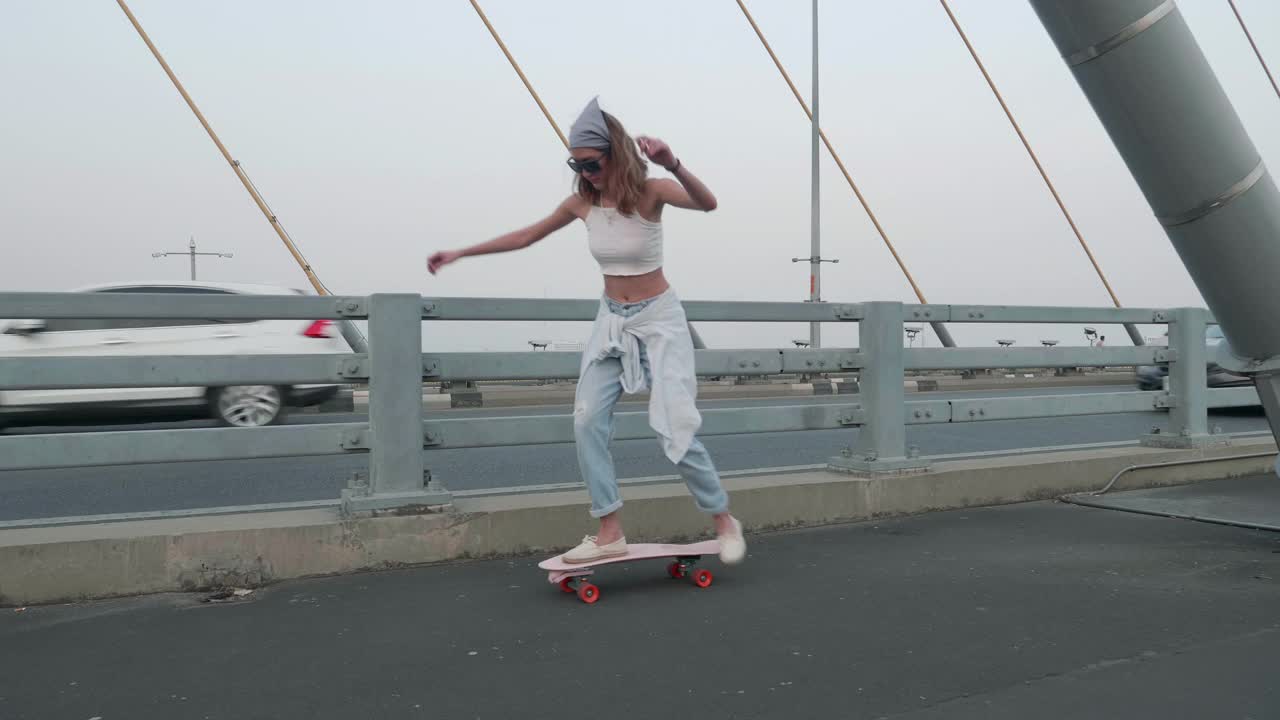 年轻时髦的亚洲女人在晚上的桥上玩滑板;慢动作视频下载