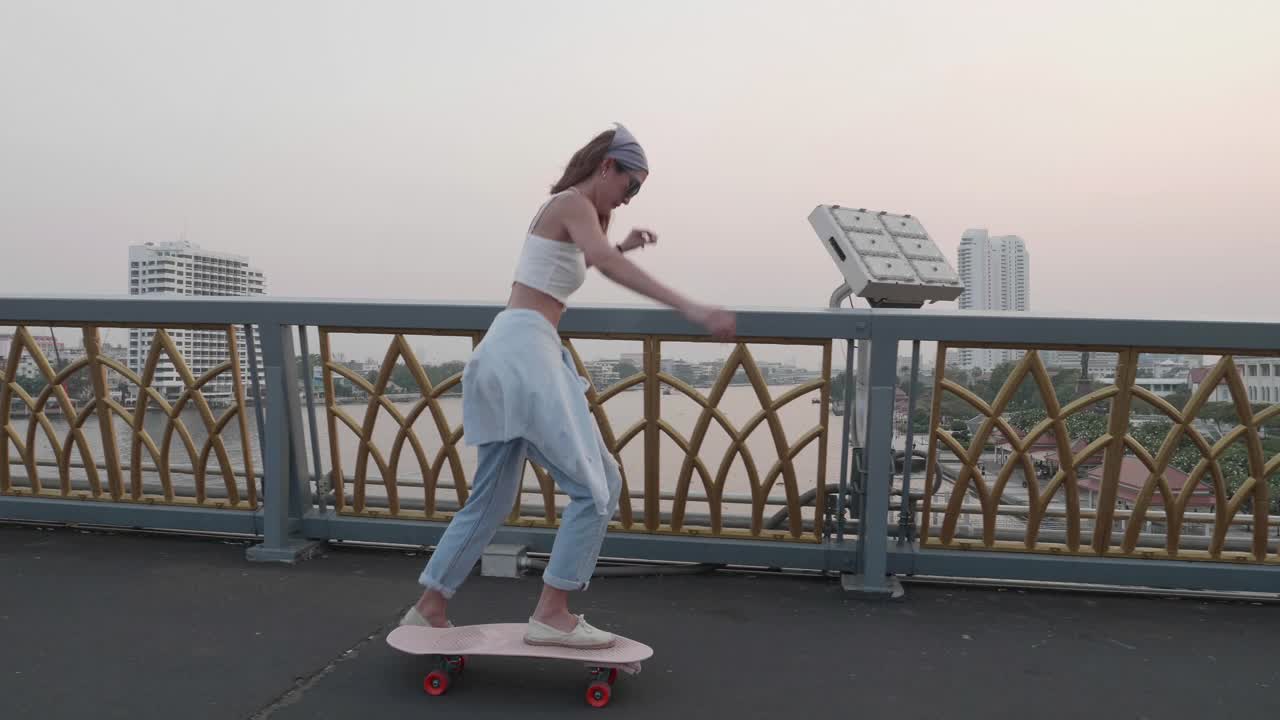 年轻时髦的亚洲女人在晚上的桥上玩滑板;慢动作视频素材