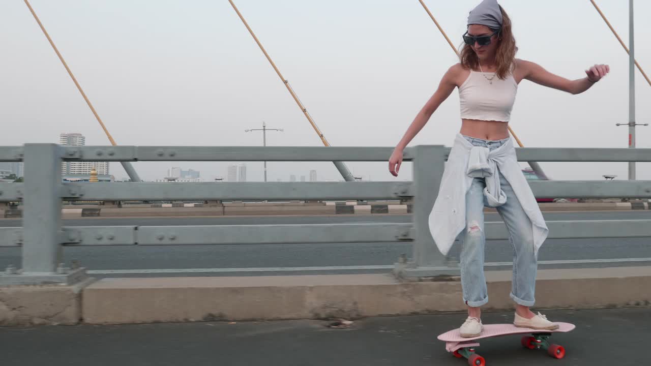 年轻时髦的亚洲女人在晚上的桥上玩滑板视频素材