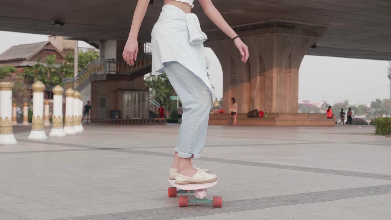 年轻时髦的亚洲女性在桥下的公园玩滑板;慢动作视频素材