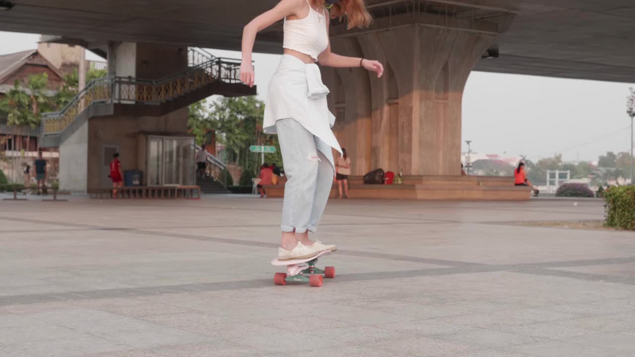 年轻时髦的亚洲女性在桥下的公园玩滑板;慢动作视频下载