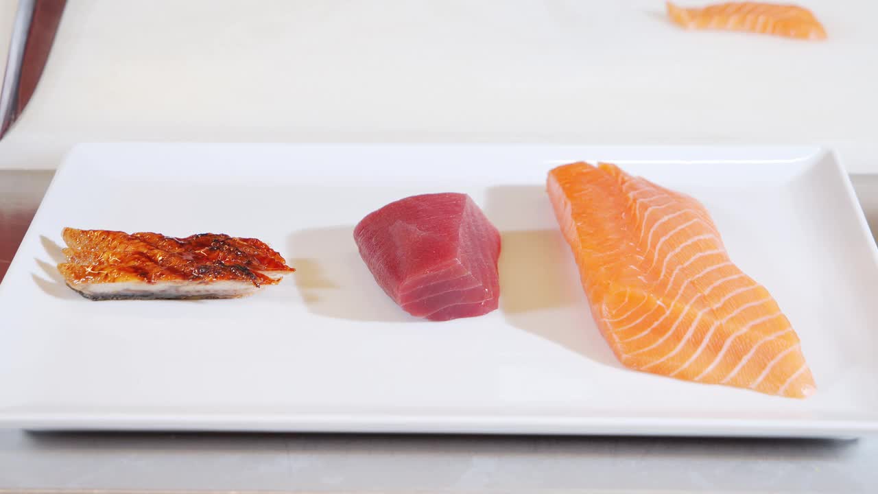 男性厨师的特写镜头从盘子里拿起新鲜的金枪鱼片。烹饪寿司卷或生鱼片视频素材