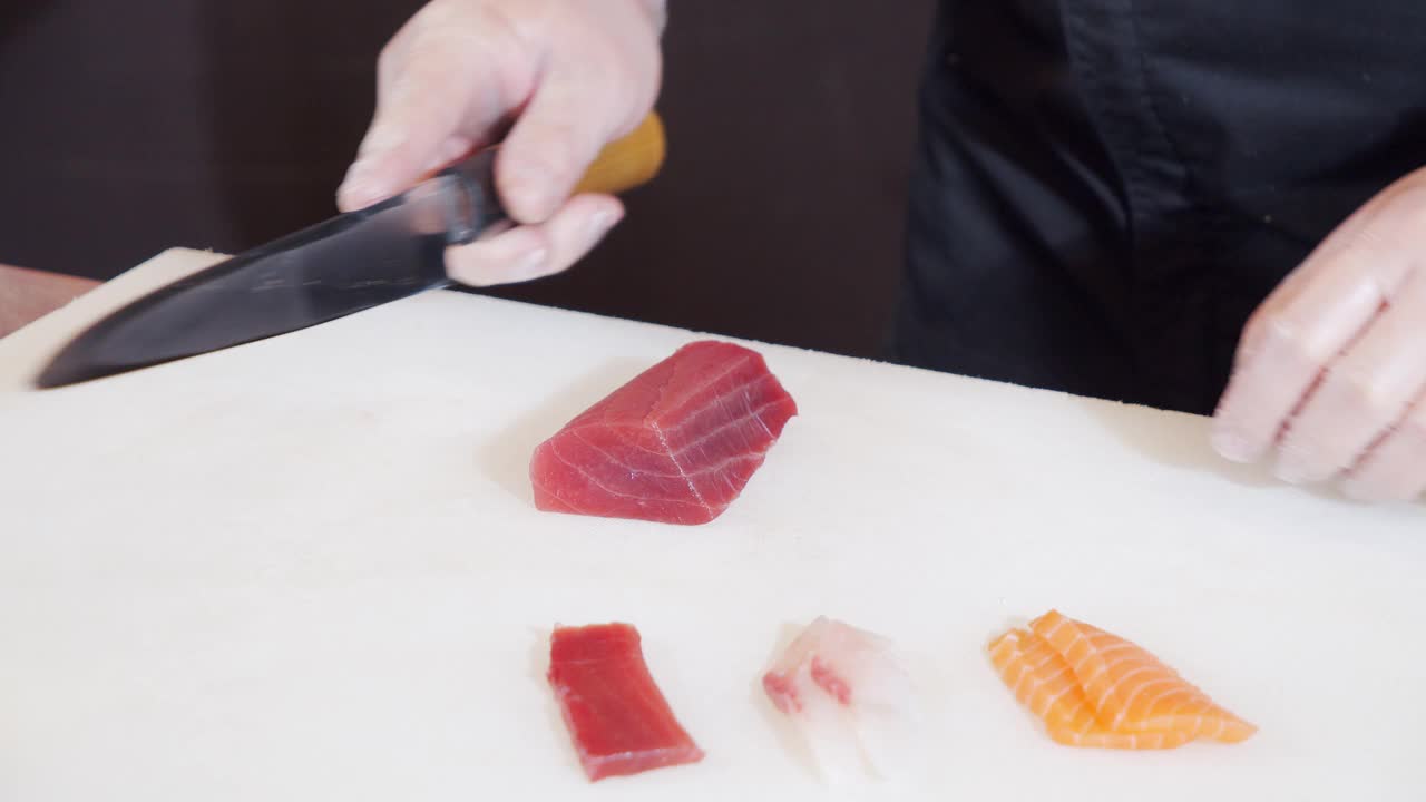 特写男厨师双手戴着手套，在白板上用刀切金枪鱼片视频素材