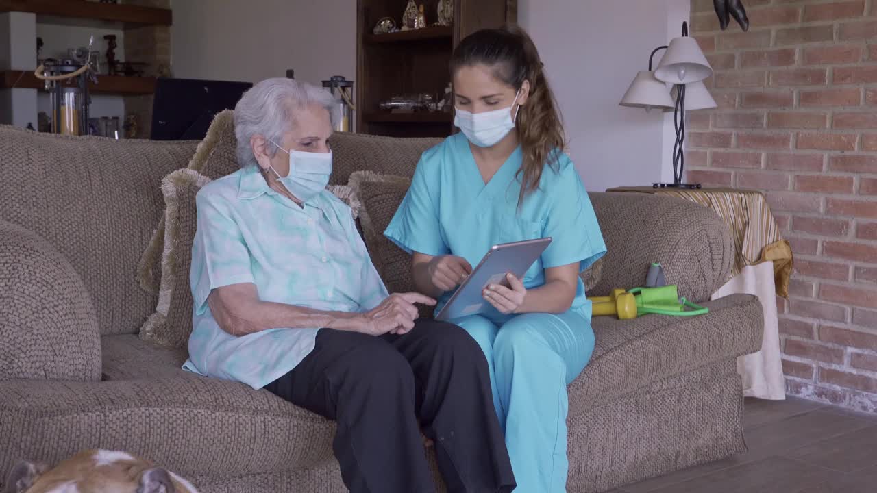 西班牙年轻护士在家里向高级妇女解释数字平板电脑的医疗结果视频下载