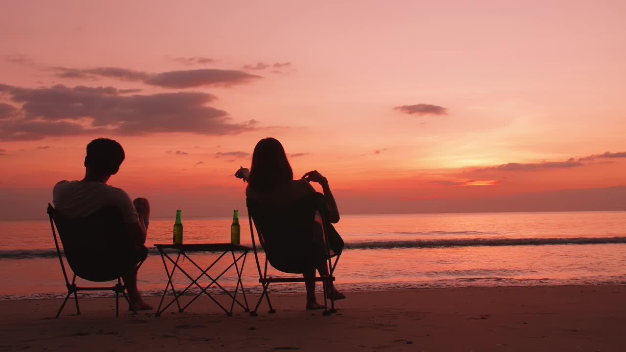 背影剪影的年轻夫妇坐在和放松在海滩上日落。视频素材
