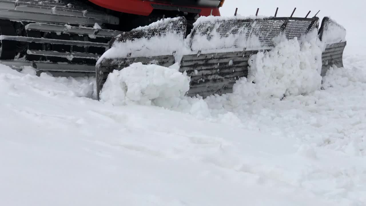 近距离的工作，宽雪车骑在雪和耙它的背景雪山。为滑雪季节和采雪准备雪坡的概念视频下载