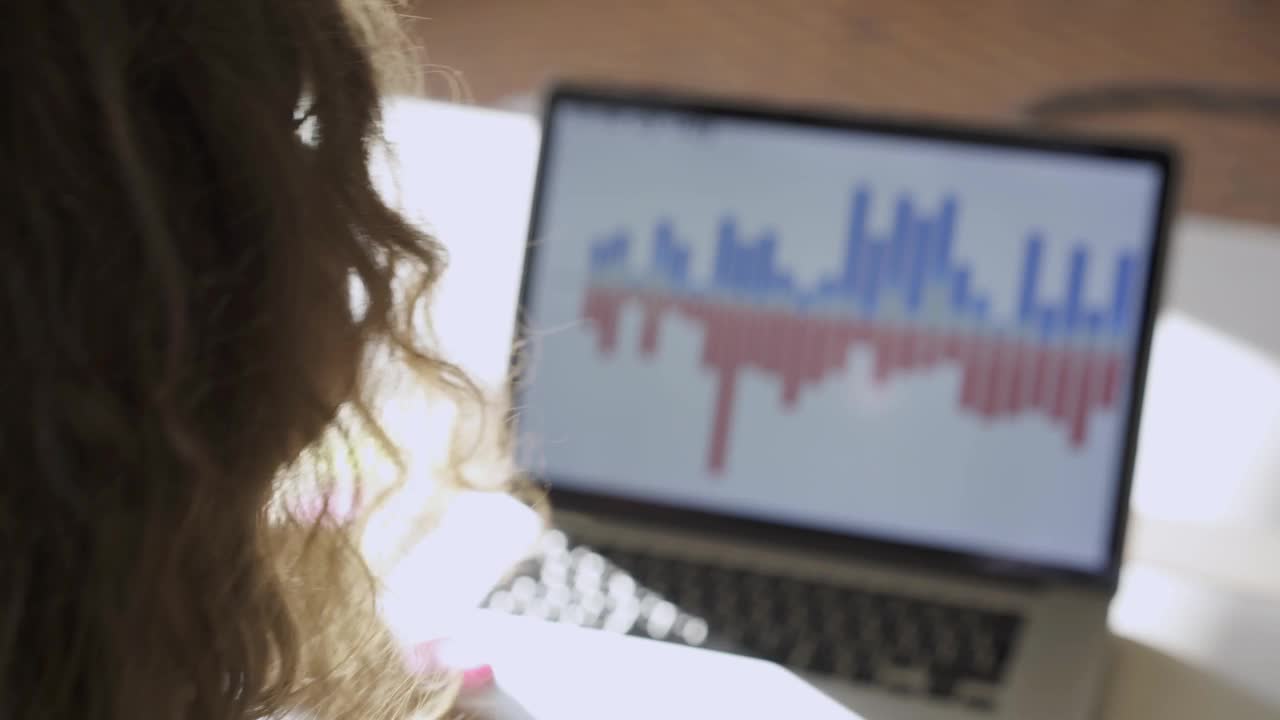一头卷发的黑发女子在笔记本电脑前戴上无线耳机视频下载