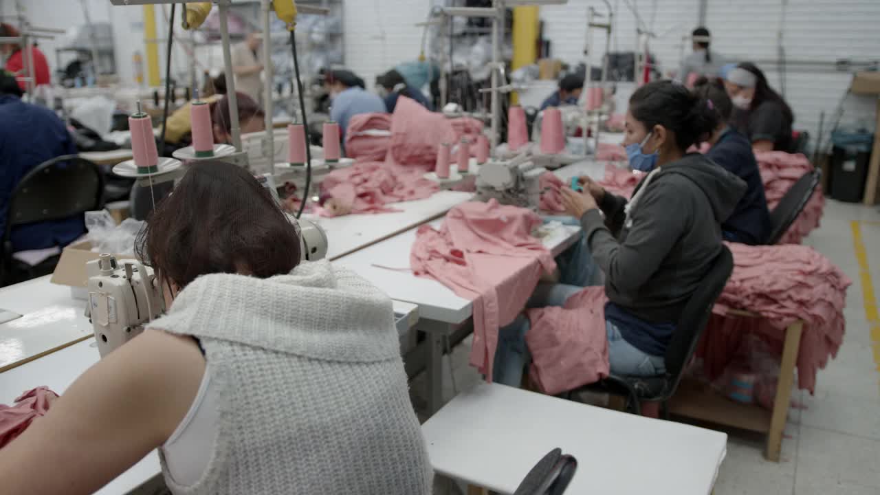 在一家服装厂的缝纫站工作的拉丁美洲妇女都戴着防护口罩视频下载