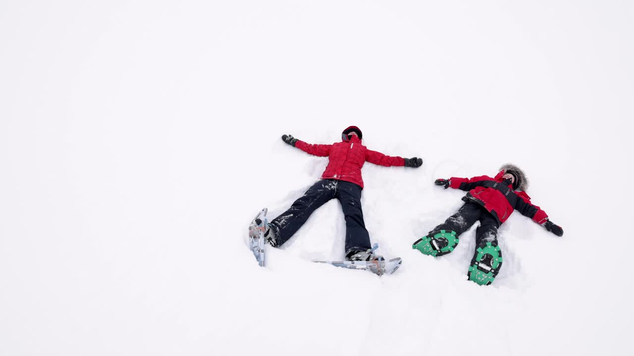 母亲和儿子在暴风雪后的雪地里做雪天使视频素材