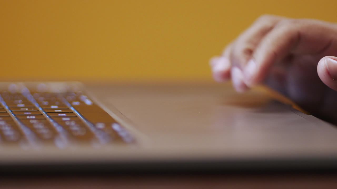 年轻的非裔美国职业女性用触控板在笔记本电脑上滚动的手指在戏剧性的灯光下，在黄芥末色的工作室背景与复制空间视频下载