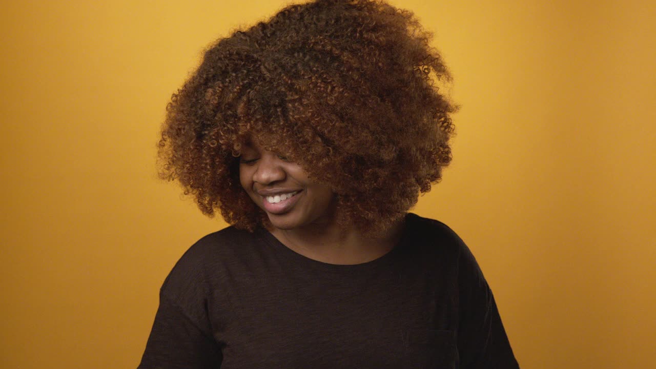 自信、美丽的年轻非洲裔美国女性在快乐的芥末黄色背景前用手持智能手机快速抓拍微笑自拍视频下载