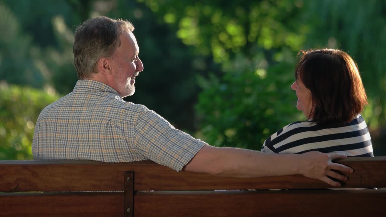 一对老年夫妇坐在夏日公园的长椅上大笑。视频素材