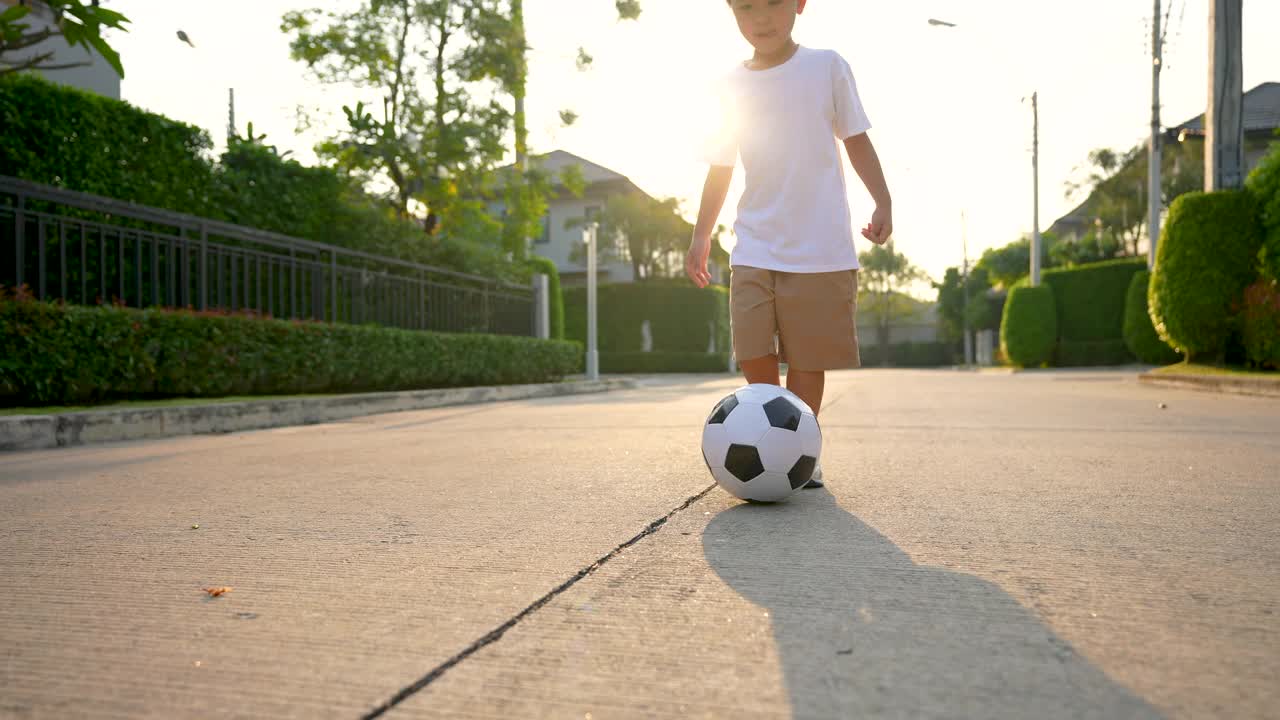 亚洲小孩在公园里踢足球，在房子的后院。假期和健康的概念视频素材