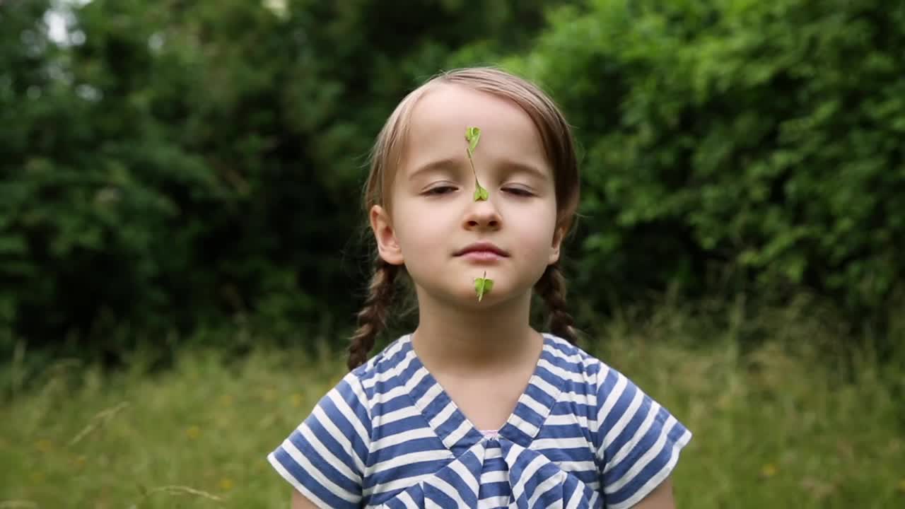 夏天，无忧无虑的女孩在花园里把绿色的直升机种子粘在脸上视频素材