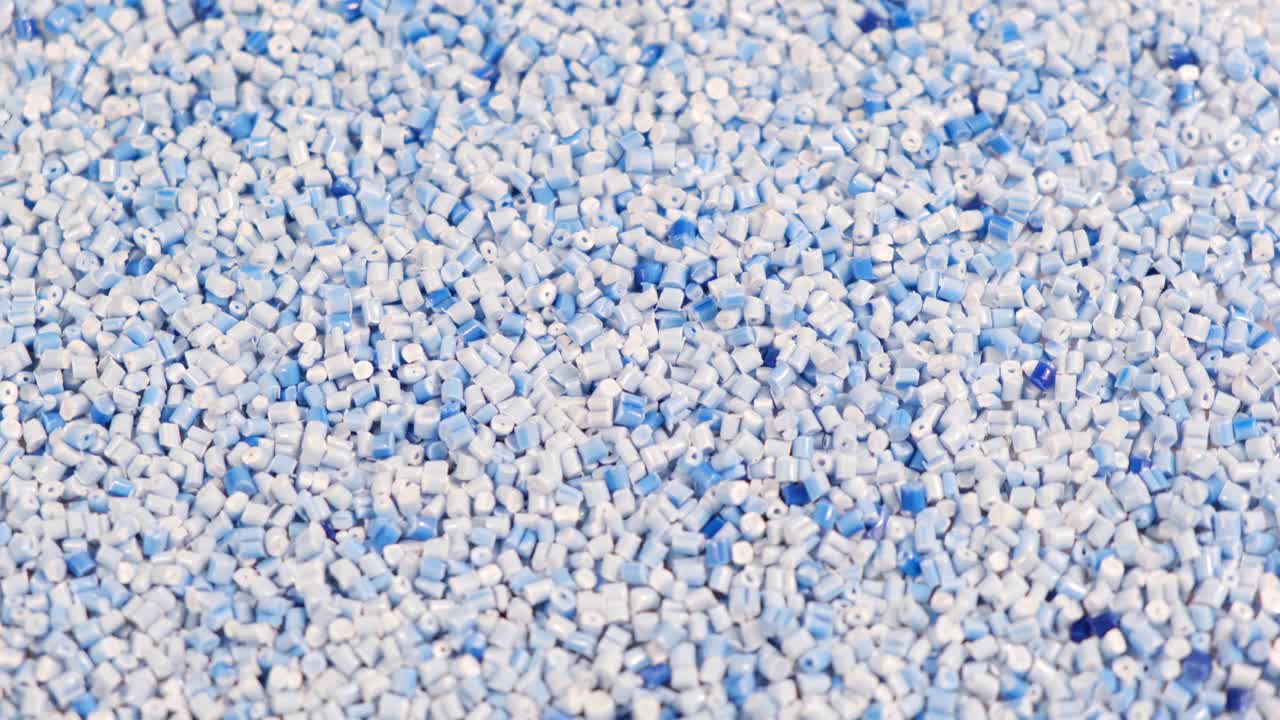 二级颗粒由聚丙烯制成，浅蓝色的塑料颗粒破碎到桌子上。工业用塑料颗粒原料。聚合物树脂。原塑料回收概念。视频素材