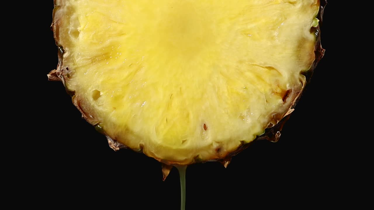 鲜榨的菠萝汁从成熟的黄色水果片近距离在一个黑色的背景慢动作视频素材