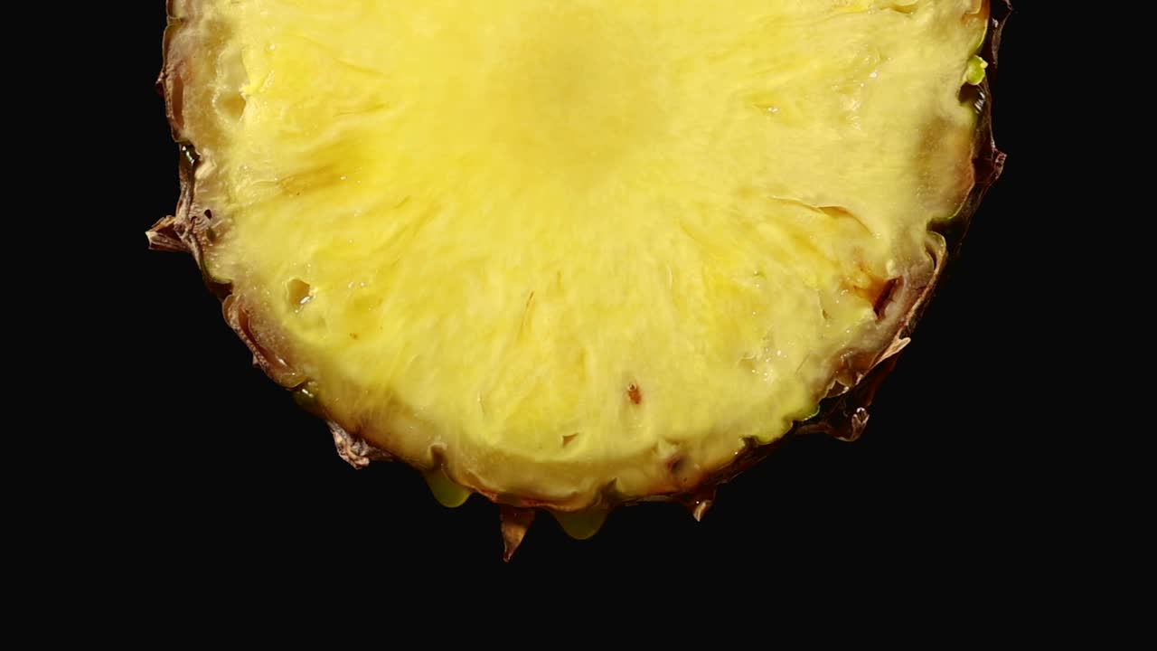 鲜榨菠萝汁滴从成熟的黄色水果片近距离在一个黑色背景慢镜头放大视频素材