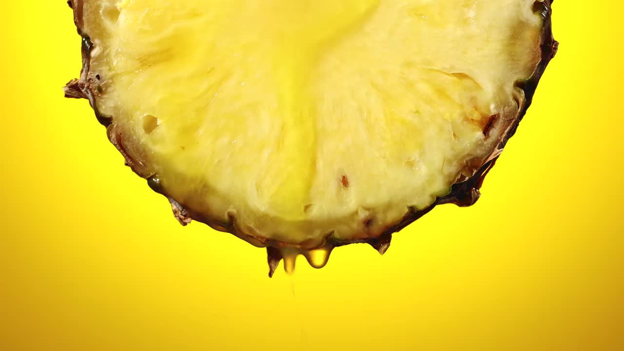 鲜榨的菠萝汁从成熟的水果片近距离在一个黄色的背景慢动作视频素材
