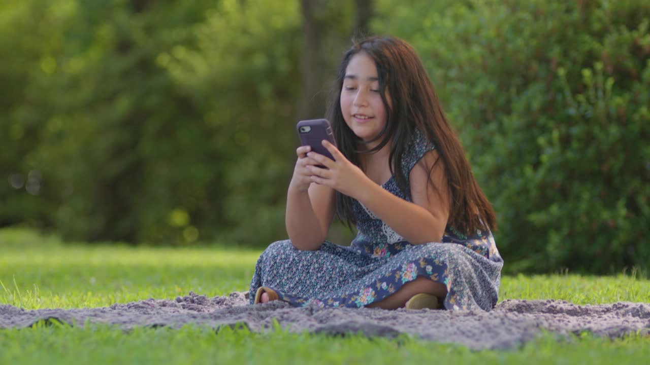 可爱的小女孩在户外玩她的智能手机视频素材
