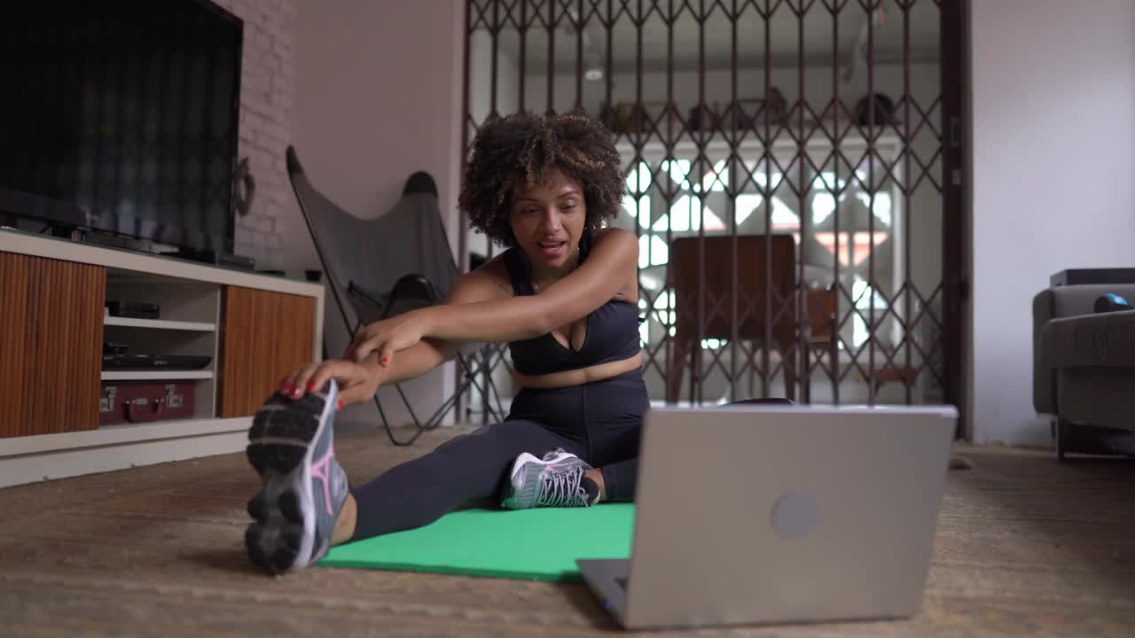 年轻女子在家里用笔记本电脑做伸展运动视频素材