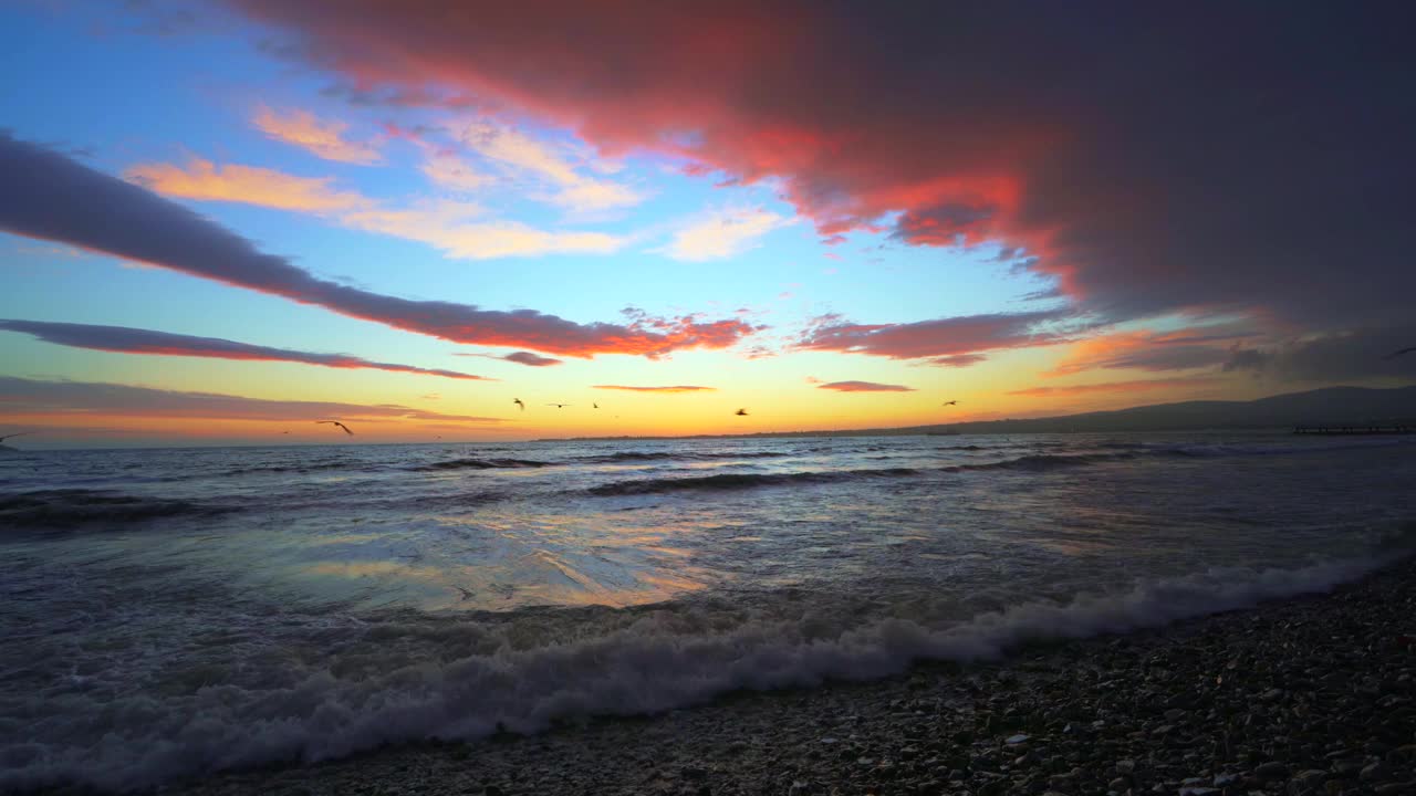 日落海景与飞鸟。从海岸观看溅起的海浪。美丽戏剧性的天空与云景视频素材