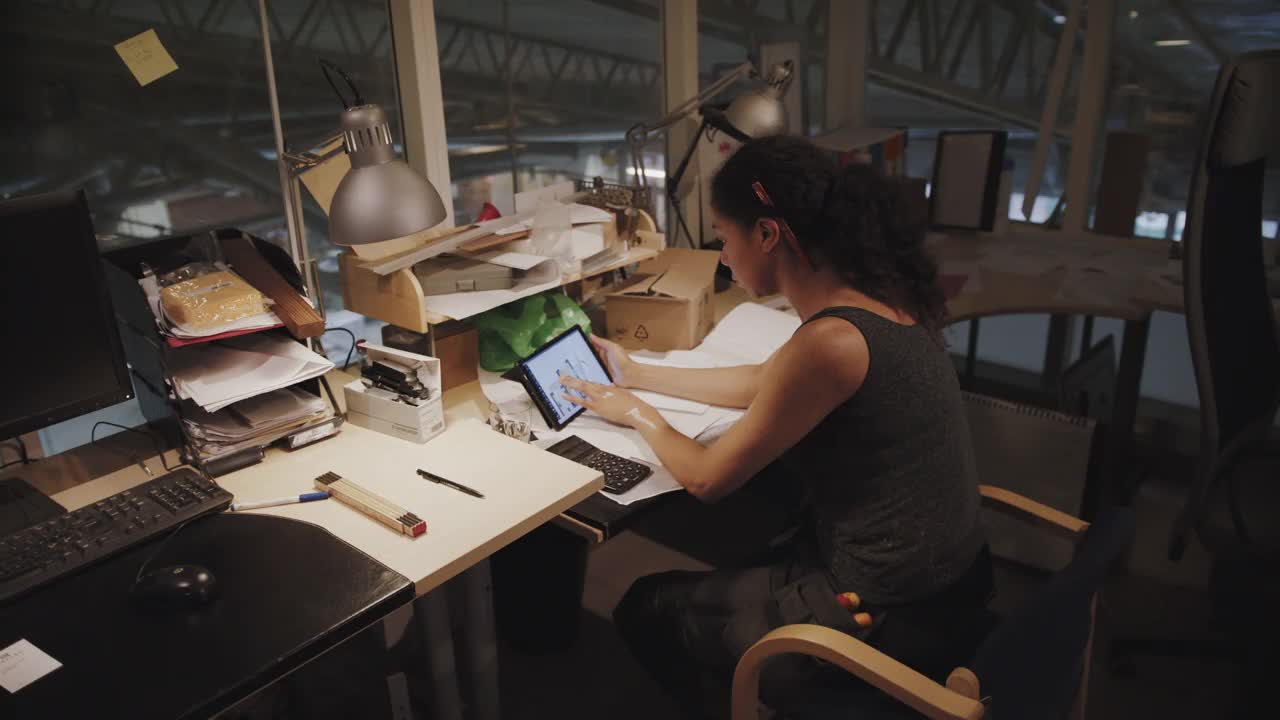 手持式拍摄的女工匠使用计算器，同时分析在车间的数字平板电脑上的设计视频下载
