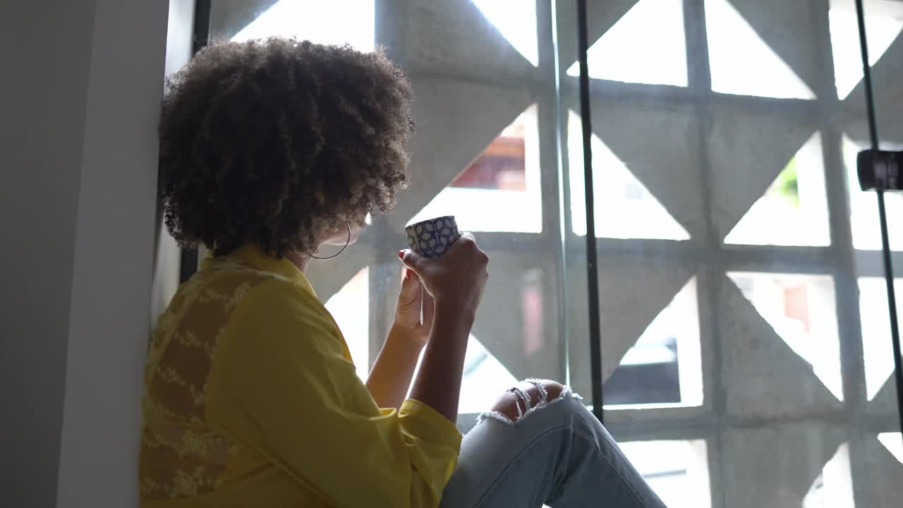 年轻女子坐在窗台上望着别处，在家里喝茶视频下载