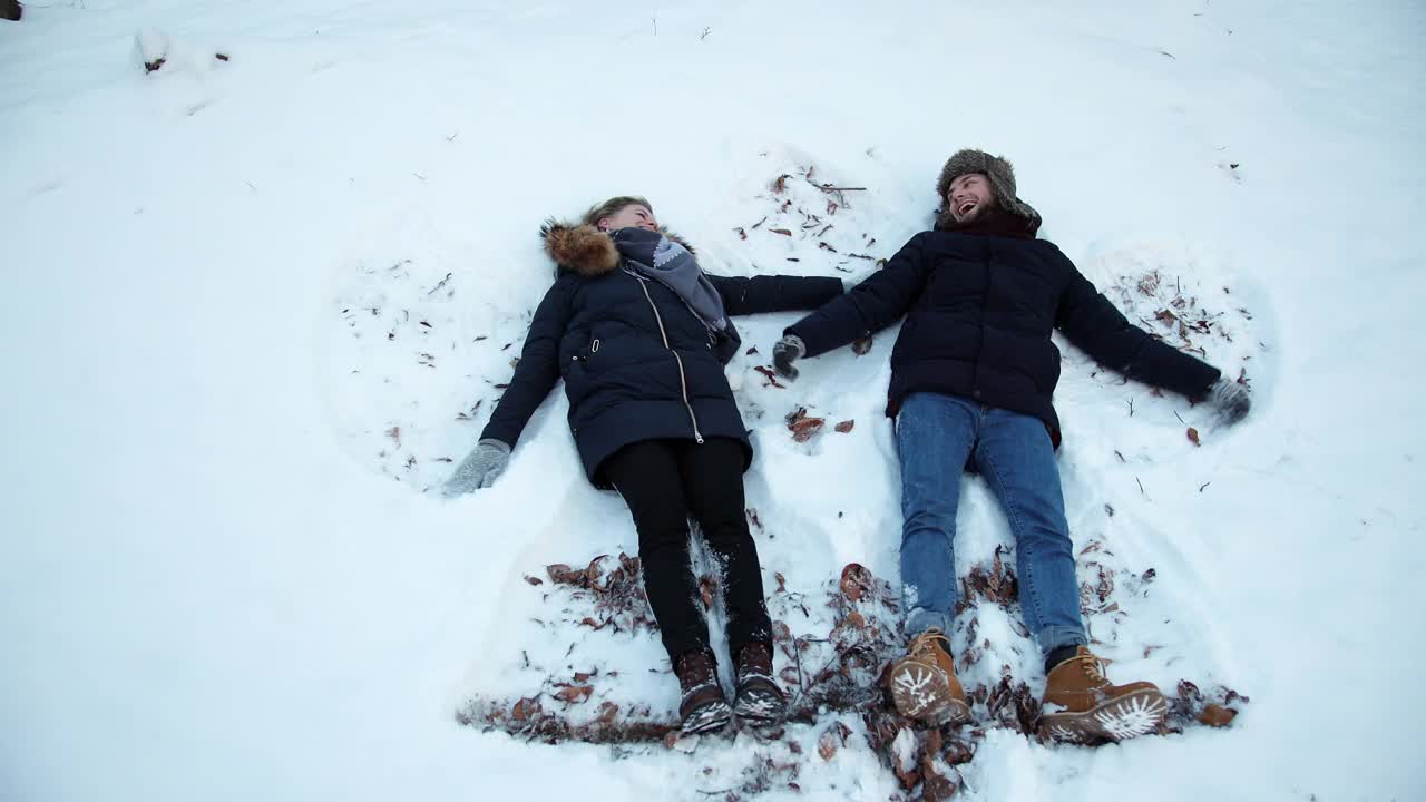 一个女孩和一个男孩躺在雪地上。躺在雪地里，动胳膊，动腿，视频素材