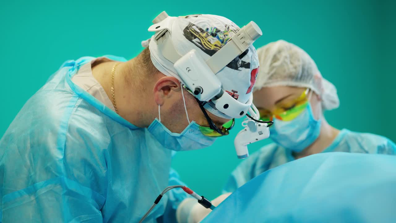 医生给病人动手术。护士在手术室帮助专科医生。一位男性外科医生在头部使用现代医疗设备进行手术的侧视图。视频下载