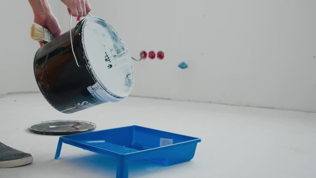 一个男人从桶里倒白漆到施工托盘的特写镜头。视频素材