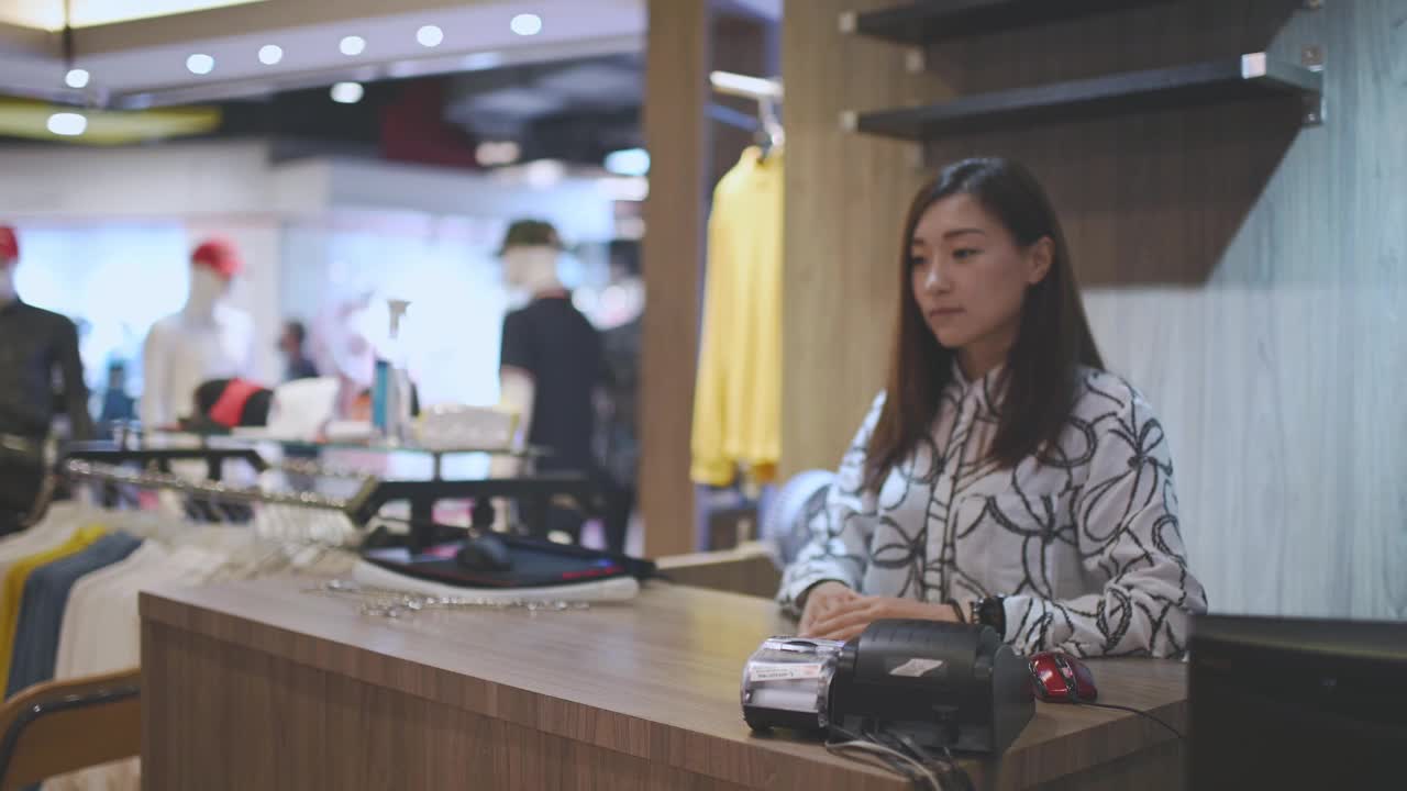 亚洲华人精品店老板接受信用卡从她的客户在收银员结账在男装店视频下载