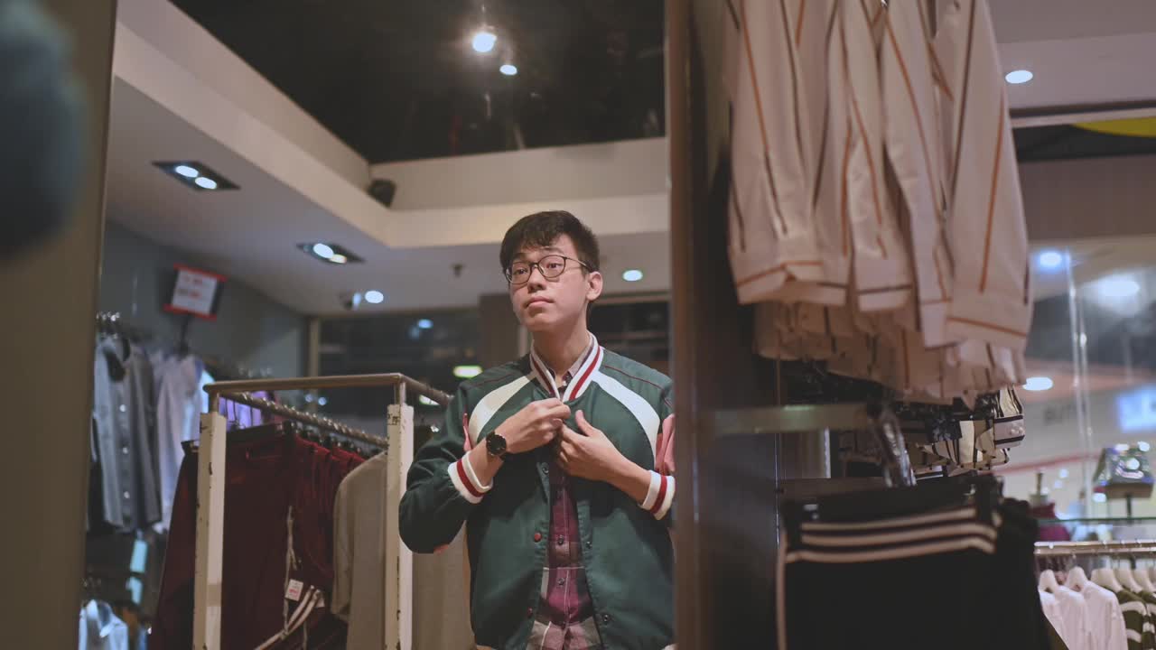 亚洲华人男性手拿男装衬衫在服装店尝试选择正确的一件购物视频下载