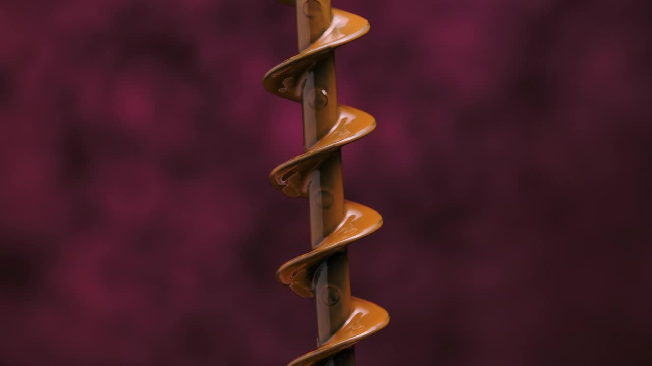 巧克力喷泉的螺旋钻旋转，并将融化的巧克力洒向不同的方向。细节与热甜甜点滴孤立在模糊的紫色背景。关闭了。慢动作视频下载