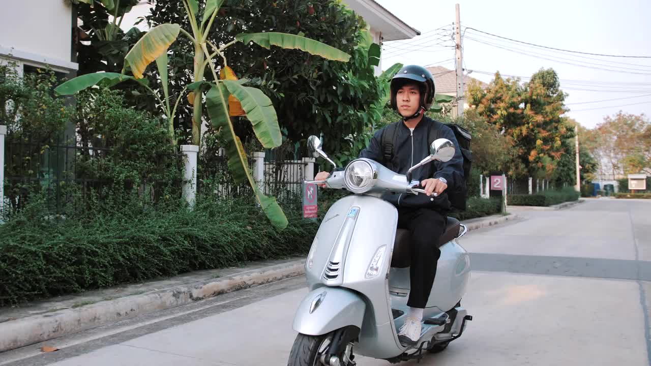 一名年轻的亚洲男子骑着一辆要送到客户家里的摩托车。视频素材