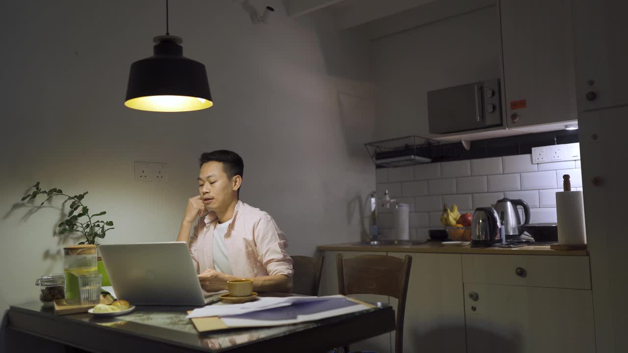 晚上加班亚洲华人男性在家里餐厅工作到很晚，情绪压力和他的财务账单在晚上单独视频下载
