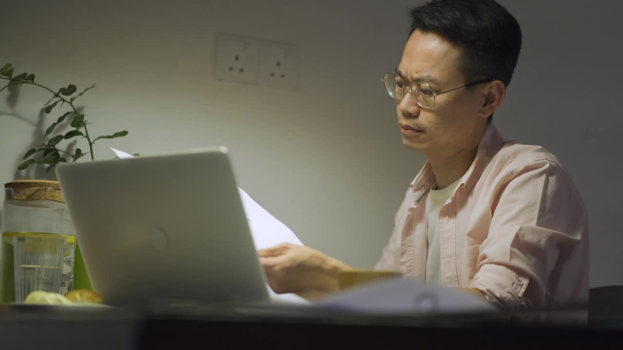 晚上加班亚洲华人男性在家里餐厅工作到很晚，情绪压力和他的财务账单在晚上单独视频下载