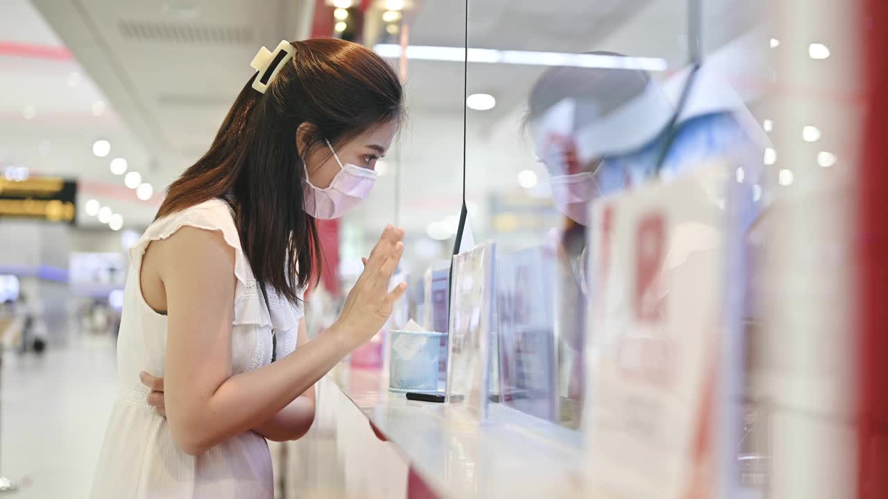 亚洲女性戴着口罩在机场柜台购买重新预订的机票，并在航班取消后自助办理登机手续视频下载