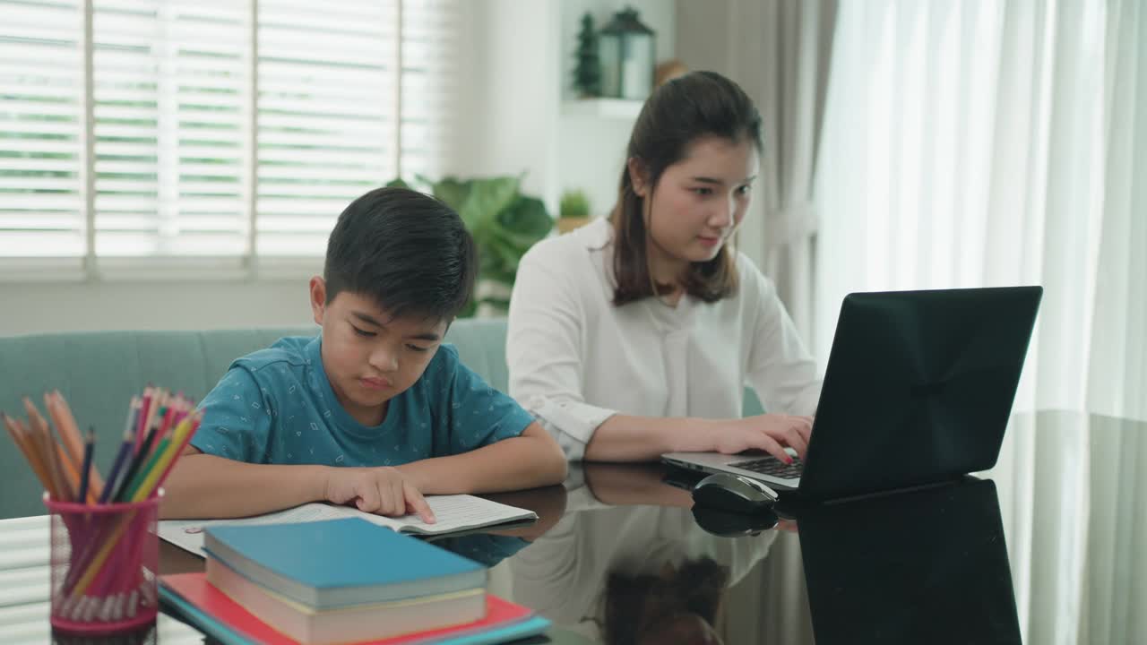 因新冠肺炎疫情学校停课期间，一位亚洲母亲与儿子并排坐在一起读书视频下载