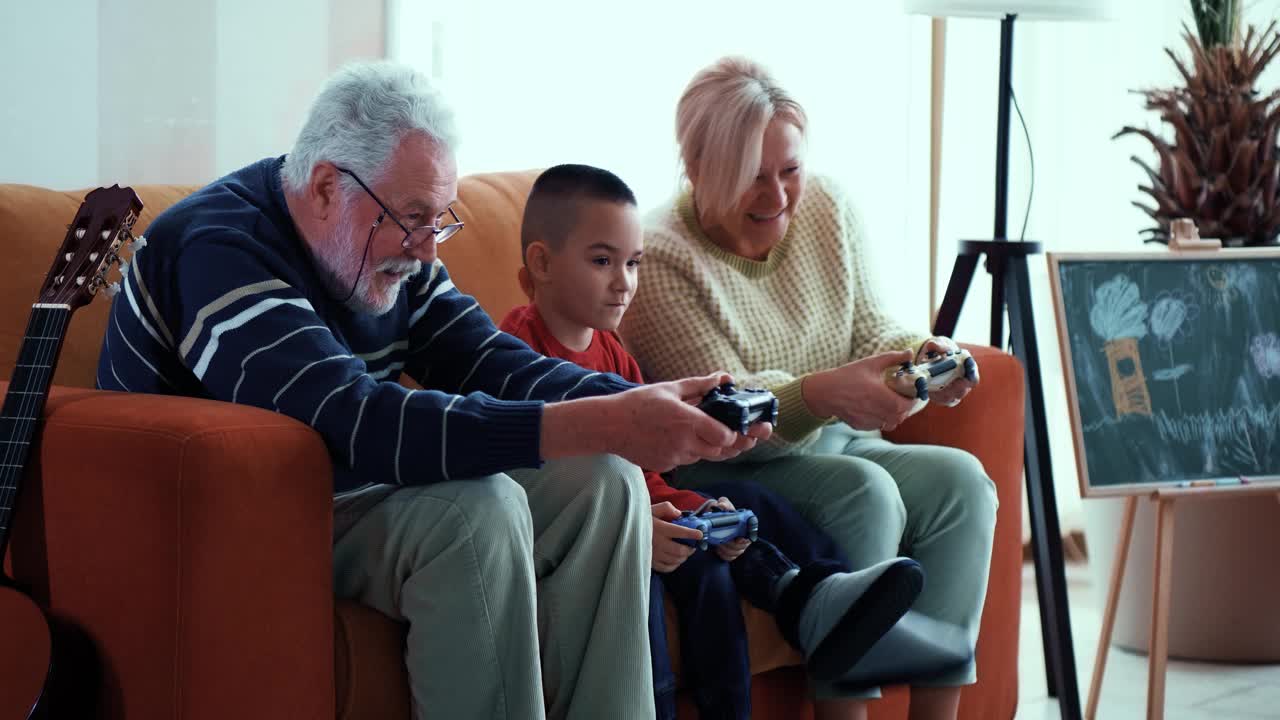 一幅快乐的孙辈和兴奋的祖父母在客厅里玩电子游戏的肖像。多代家庭在家里用一个操纵杆娱乐。视频素材