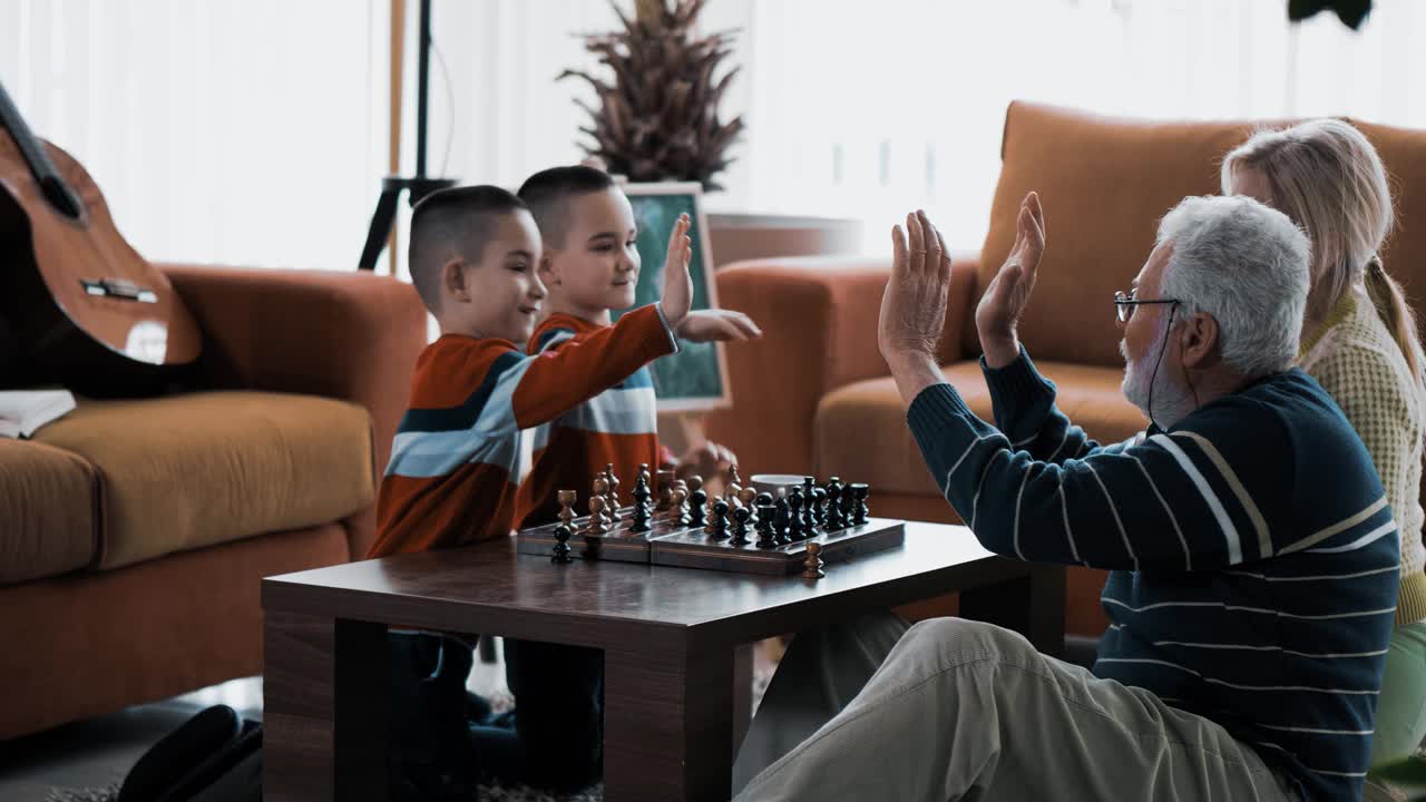 小孙子双胞胎在下象棋后给5个祖父母。祖父母在家里款待双胞胎孙子。多代，乐趣和家庭玩视频素材